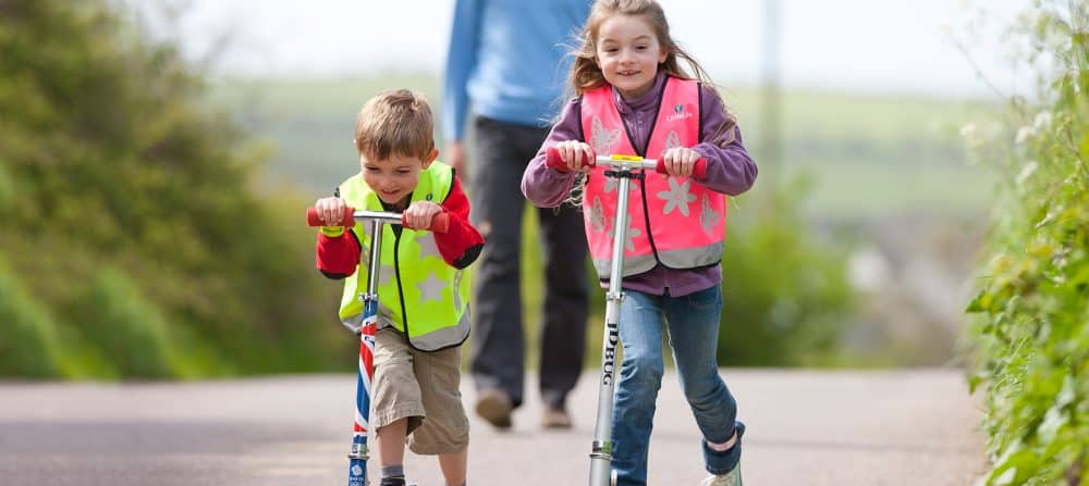Chłopak i dziewczynka z kamizelką odblaskową Littlelife, na hulajnodze.