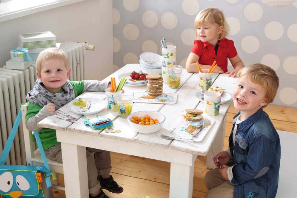 Trójka dzieci siedzi przy stole i świętuje roczek malucha.