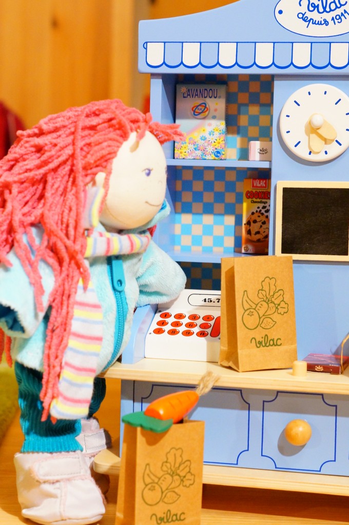 Vilac drewniany sklepik dla dzieci: zdjęcie pokazuje lalkę Lili marki Haba w zimowym stroju, obok sklepiku