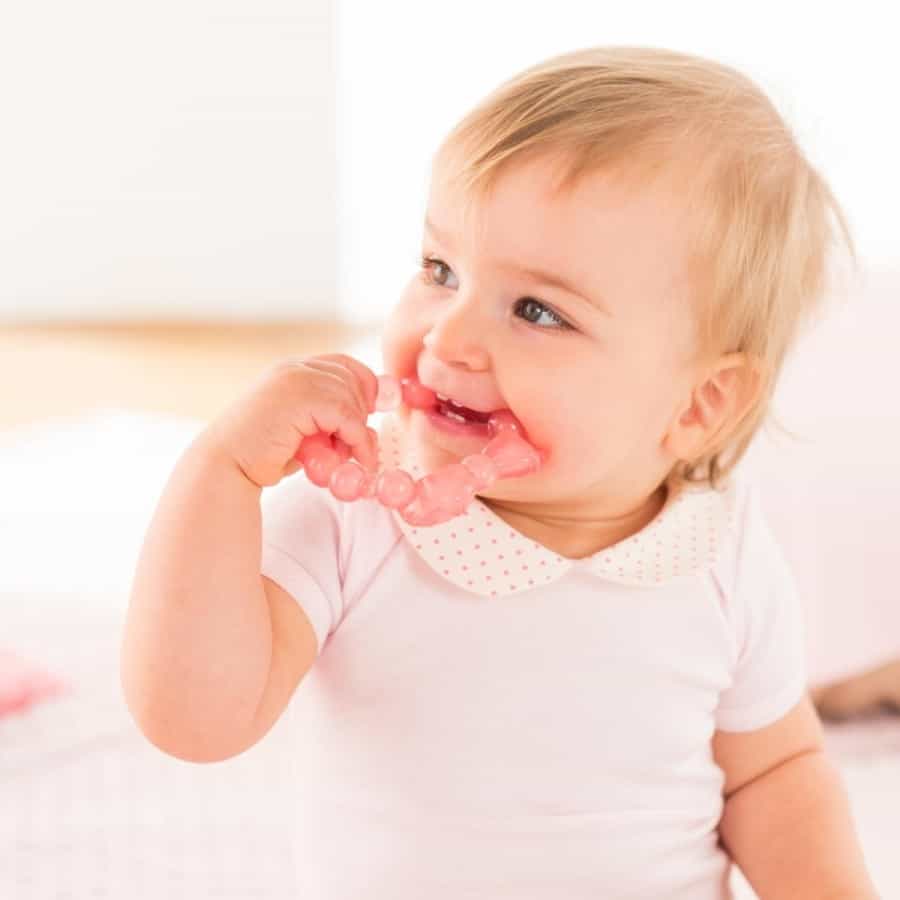 Ząbkujące dziecko z gryzakiem chłodzącym marki Corolle. Gryzak jest różowy.